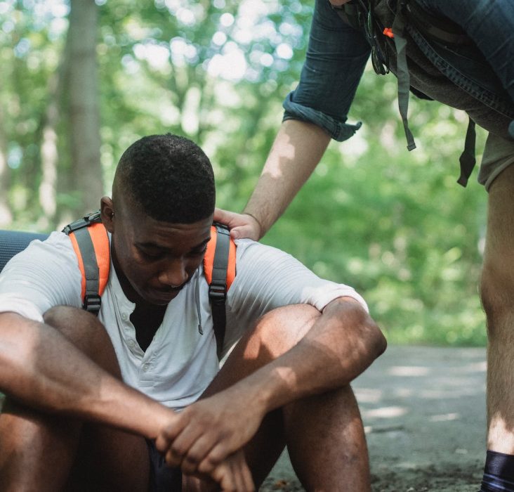 Unhappy black hiker sitting on ground in forest